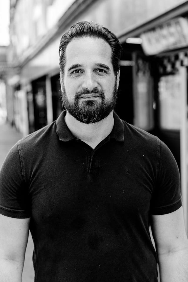 Mathias Ziehengraser, der Projekte in Schieflage übernimmt, schaut ernst und direkt in die Kamera, Schwarzweiß, hinter ihm eine unscharfe Budengasse.