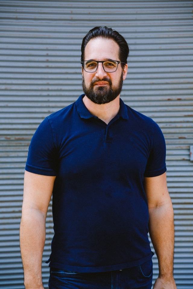 Mathias Ziehengraser mit Brille steht ruhig vor einer grauen Wellblechwand, die Arme hängen locker.